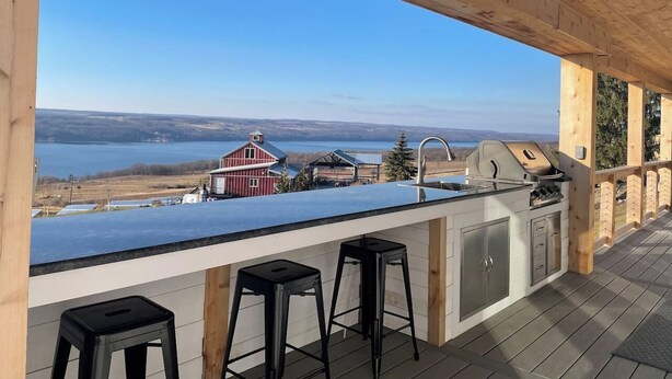 An outdoor kitchen with a view of a lake and a red barn. - VRFLX Seneca View Villa | Walk to Wineries (Burdett)