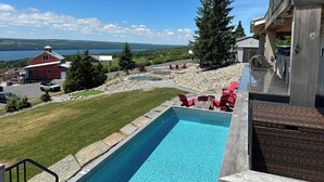 A swimming pool with a view of a lake, a red barn, and a large tree.