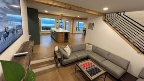 A spacious living area with a sofa, coffee table, and a TV. A wooden bench and a plant are also visible. - VRFLX Seneca View Villa | Walk to Wineries (Burdett)