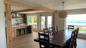 A spacious dining area with a large wooden table and chairs, a kitchen with a brick backsplash, and a view of the outdoors. - VRFLX Seneca View Villa | Walk to Wineries (Burdett)