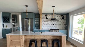 A modern kitchen with a central island, bar stools, pendant lights, and a brick backsplash. - VRFLX Seneca View Villa | Walk to Wineries (Burdett)