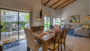 Ampla sala de estar com mesa de jantar de madeira, assentos confortáveis, sofá e uma grande janela com vista para o exterior.