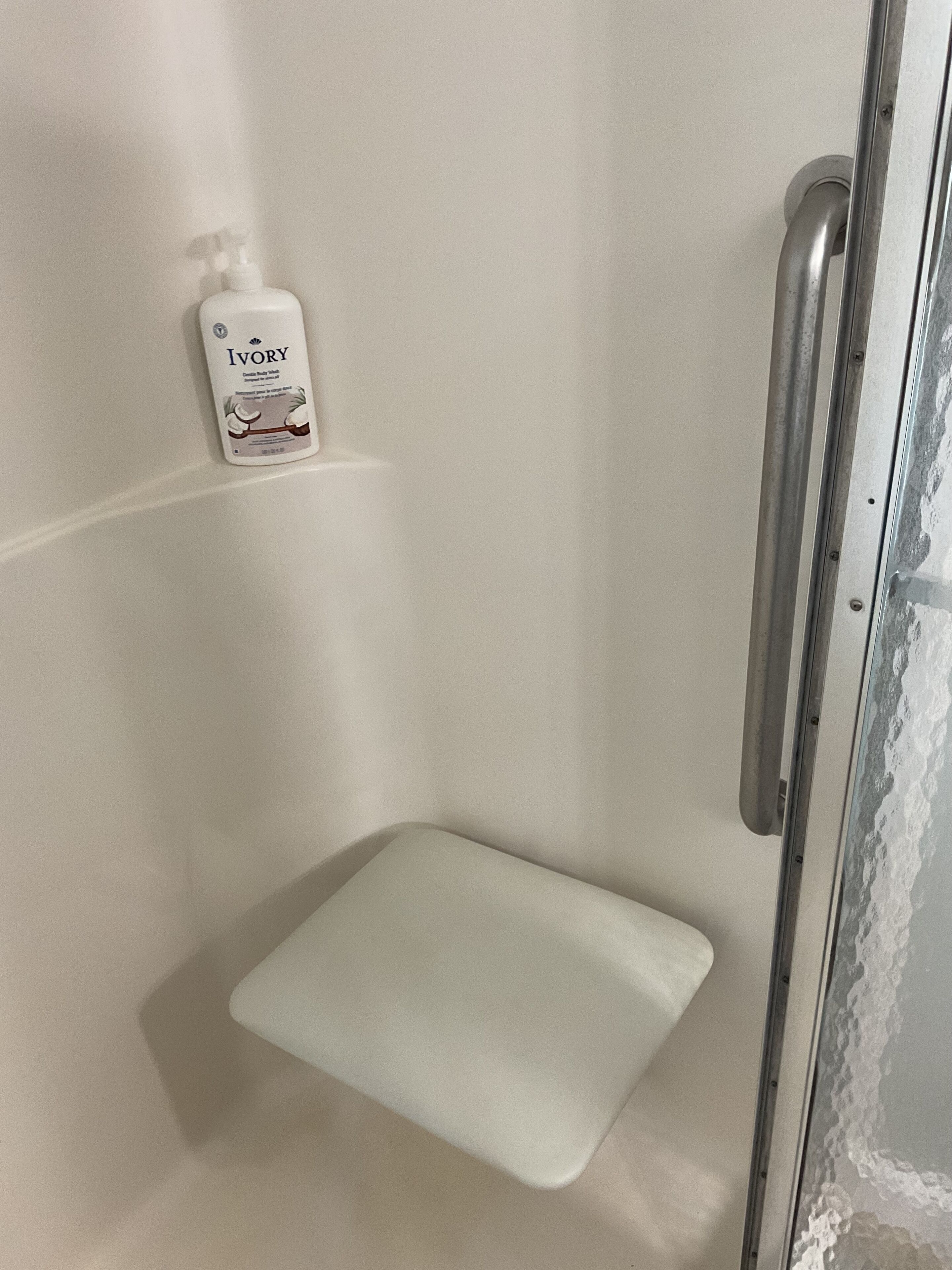 Zona de ducha con asiento blanco y una botella de Jabón Ivory en un estante.