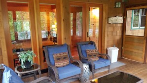 A wooden cabin interior with wicker chairs, a small table, and a potted plant. - McKenzie Riverfront Cabin big screened-in porch, 1/2mi to Mckenzie River Trail (McKenzie Bridge)