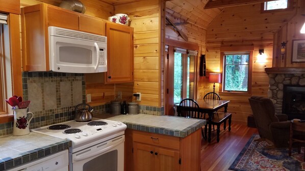 A wooden cabin kitchen with a stove, microwave, and tiled backsplash. - McKenzie Riverfront Cabin big screened-in porch, 1/2mi to Mckenzie River Trail (McKenzie Bridge)
