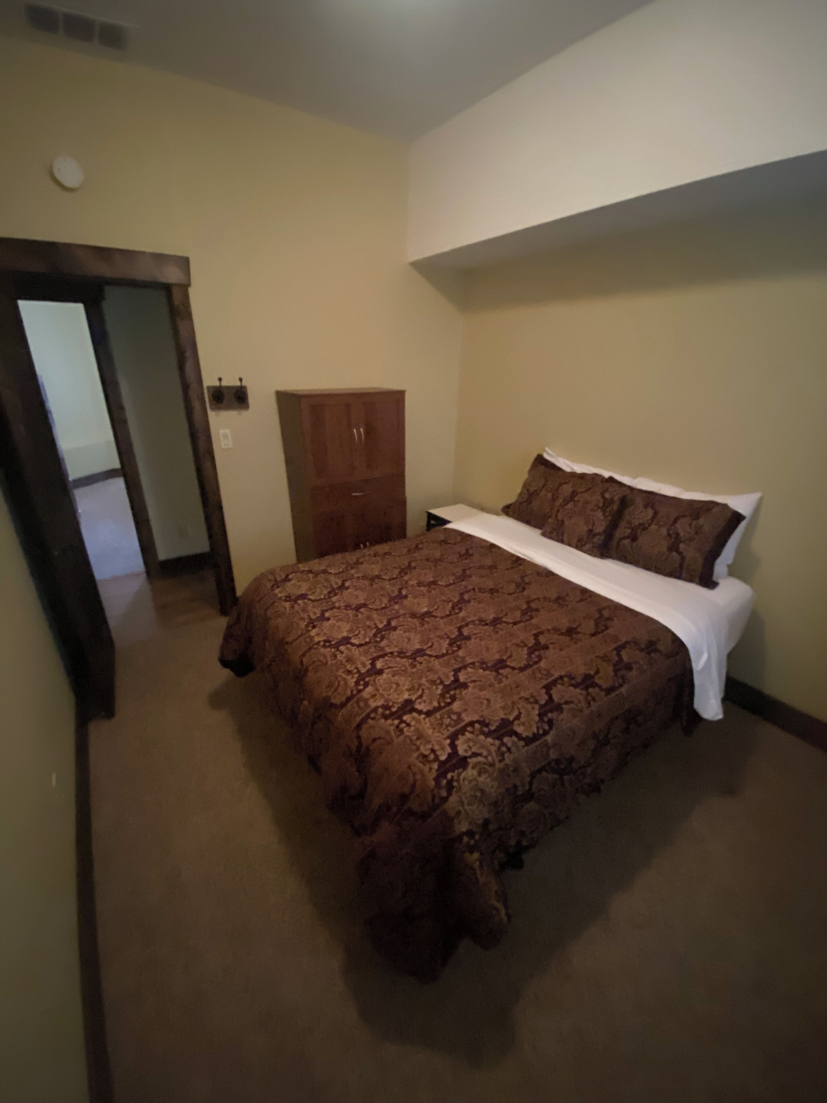 A bedroom with a large bed, a wooden wardrobe, and a door leading to another room.