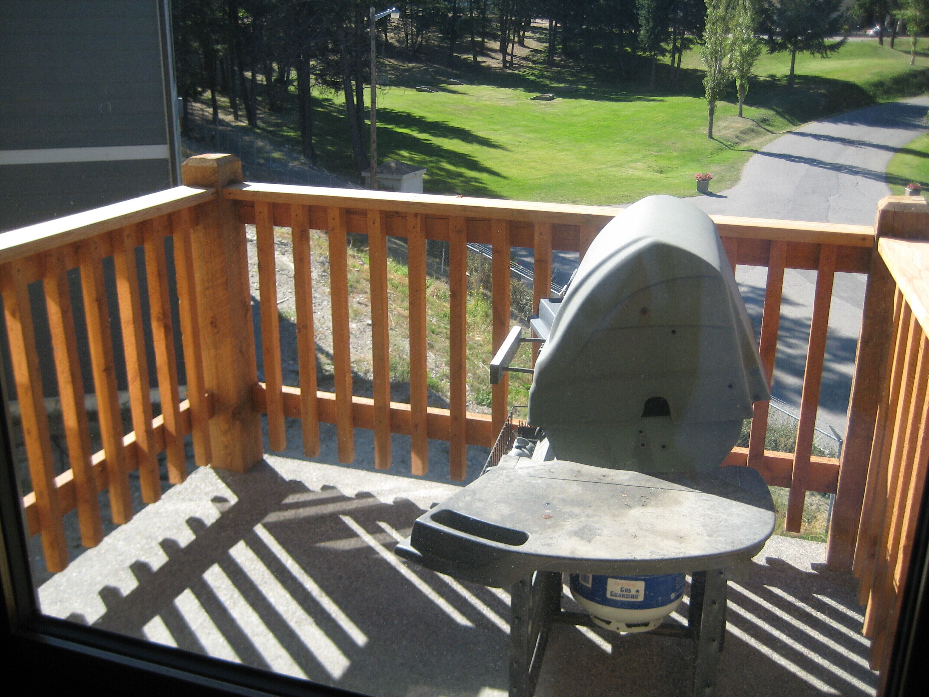 A balcony with a grill and a table, overlooking a green landscape and a road.
