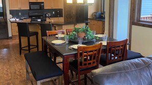 A modern kitchen with wooden cabinets, a black countertop, and a dining area with a black leather couch and wooden chairs. - Luxury Walk Out House in Radium Hot Springs 5 Bedrooms (Radium Hot Springs)