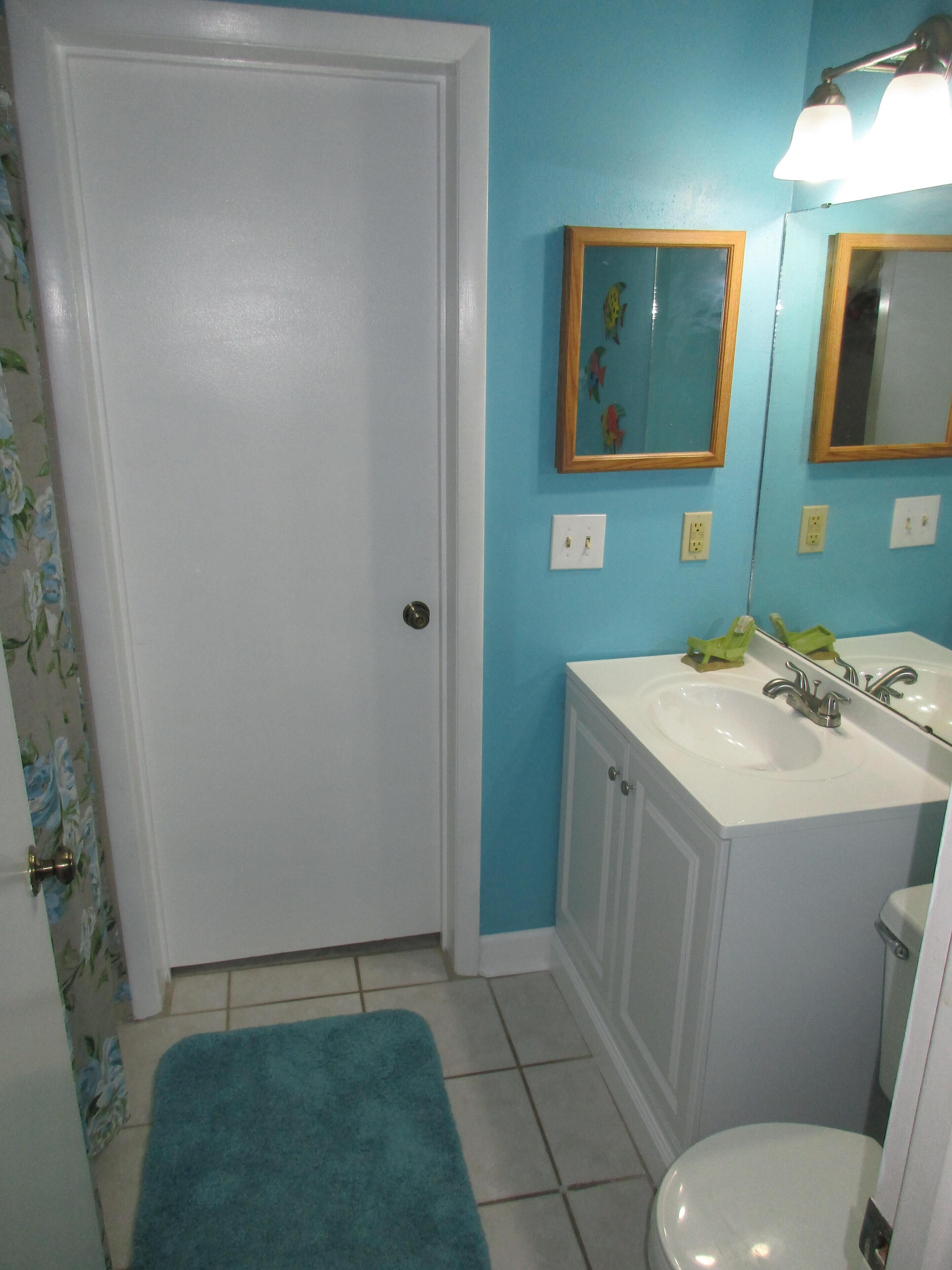 Une salle de bain avec un lavabo blanc, des toilettes, un mur bleu et une porte.