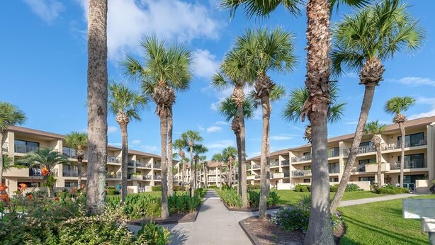 A hotel with a central pathway flanked by palm trees, leading to a building with multiple balconies. - 2 Bedroom Ocean View Condo, walk to restaurants/bars, 2 pools on premises (St Augustine)