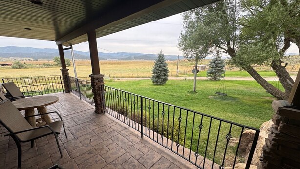 A covered patio with stone flooring and metal railings, overlooking a grassy landscape with trees and distant hills. - Remote ranch house on 93 acres in the peaceful Indianola Valley! Sleeps 30 (Fairview)