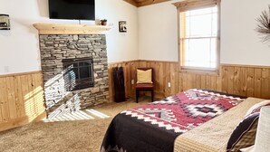 A bedroom with a stone fireplace, wooden ceiling, and a bed with a patterned blanket. - Remote ranch house on 93 acres in the peaceful Indianola Valley! Sleeps 30 (Fairview)