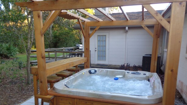 A wooden hot tub with a wooden deck and steps, surrounded by a wooden pergola.