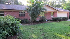 A single-story brick house with a garage, surrounded by a well-maintained lawn and various shrubs.
