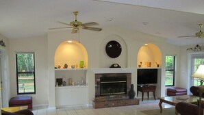 A living room with a fireplace, a television, and a ceiling fan.