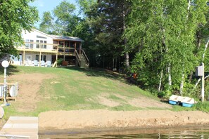 Enjoy serene lakeside living with a two-story house, deck, and staircase, surrounded by lush greenery and a dock.