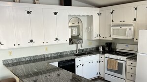 Een moderne keuken met witte kasten, een granieten aanrechtblad, een inbouwoven en een magnetron.