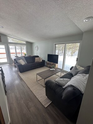 Relax in this serene space with a sofa, armchair, and flat-screen TV, offering a peaceful view of the surrounding landscape.