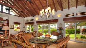 A spacious dining area with wicker furniture, a glass table, and a view of the outdoors.