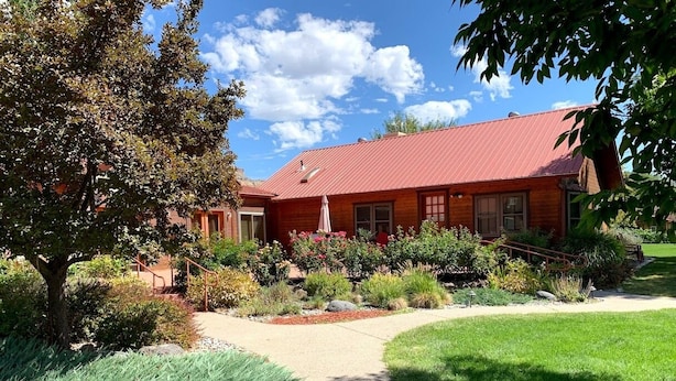 Una casa de ladrillo con techo rojo, rodeada de un jardín cuidado con diversas plantas y un camino de grava que lleva a la entrada.