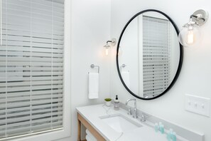 Un bagno moderno con un lavandino bianco, uno specchio con cornice nera e un porta asciugamani.