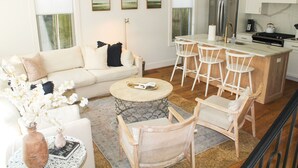 A modern living room with a sofa, chairs, a coffee table, and a kitchen area with a refrigerator and stove. - Guesthouse Charleston: WEST (242 B) (Charleston)