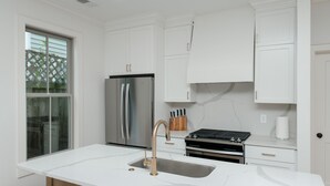 A modern kitchen with white cabinetry, a stainless steel refrigerator, a gas stove, and a marble countertop. - Guesthouse Charleston: WEST (242 B) (Charleston)