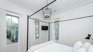 A bedroom with a bed, white curtains, a black floor lamp, and a TV on the wall. - Guesthouse Charleston: WEST (242 B) (Charleston)