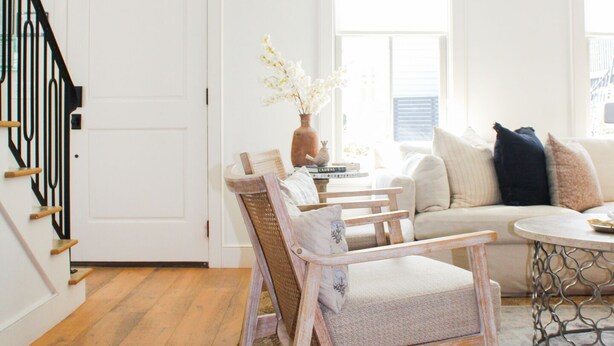 A cozy living room with a wooden staircase, a sofa, a coffee table, and a dining area with wicker chairs and a vase of flowers. - Guesthouse Charleston: WEST (242 B) (Charleston)
