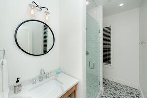 A bathroom with a round mirror, a white sink, and a glass-enclosed shower area.
