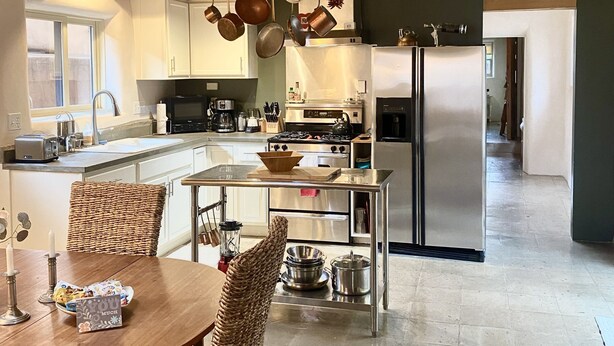 A kitchen with wooden beams, a dining area with wicker chairs, and stainless steel appliances.