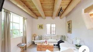 A cozy living room with a wooden ceiling, a white sofa, a coffee table, and a window with curtains.
