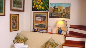 Una habitación con un sofá color beige, dos almohadas, una lámpara y un cuadro enmarcado de un paisaje urbano.