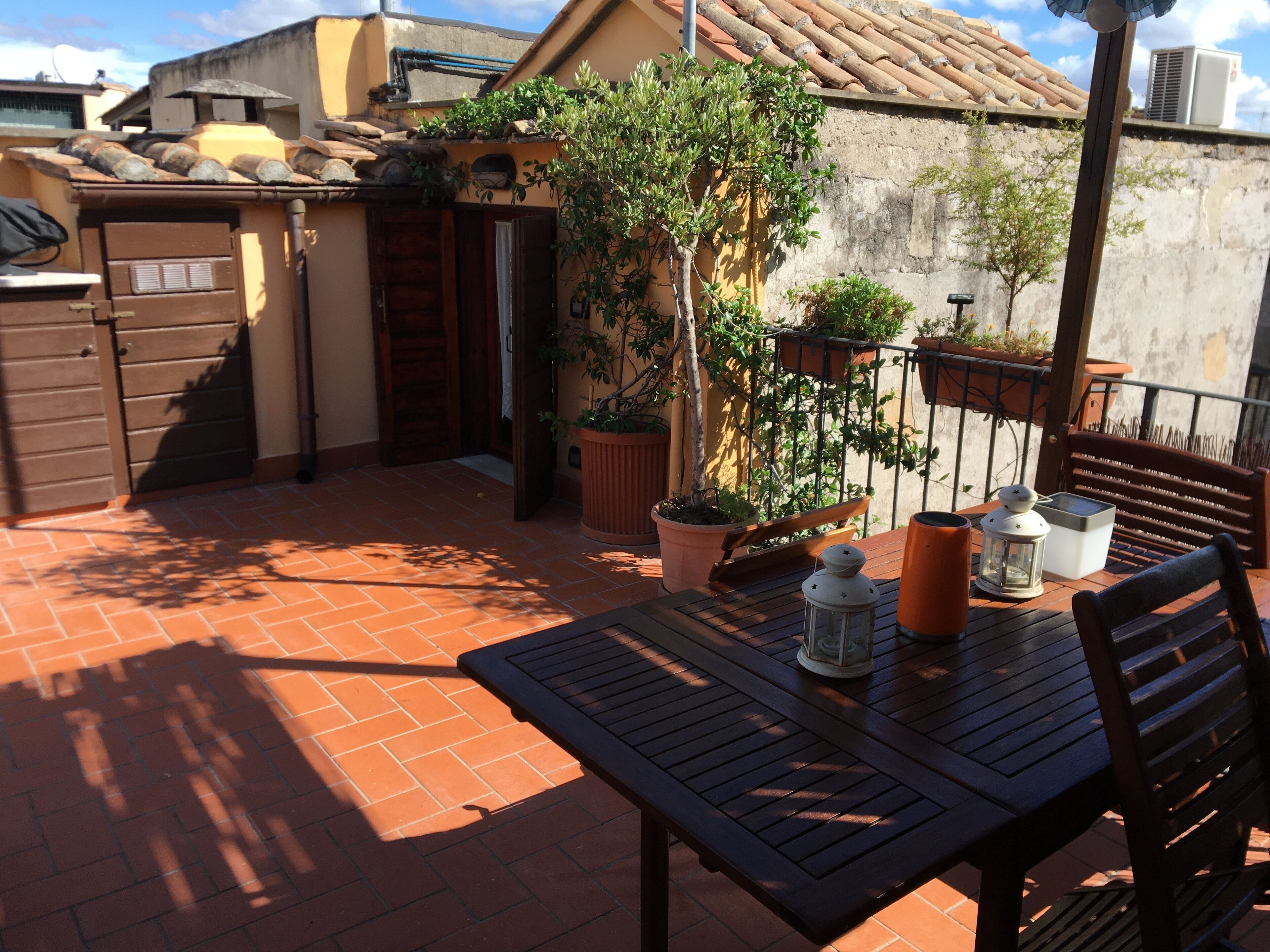 A patio with a table and chairs, potted plants, and a wooden bench.