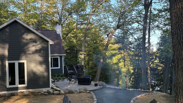 A cabin with a fire pit area, surrounded by trees and outdoor seating. - Beautiful Cottage on Private Lake close to Manistee  (Wellston)