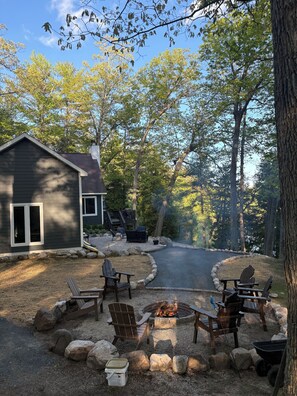 A cabin with a fire pit area, surrounded by trees and outdoor seating. - Beautiful Cottage on Private Lake close to Manistee (Wellston)