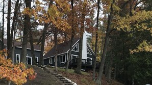 A house with a stone pathway leading to a wooden deck, surrounded by trees with autumn leaves. - Beautiful Cottage on Private Lake close to Manistee  (Wellston)