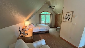 A bedroom with a bed, a nightstand, a desk, a chair, a ceiling fan, and a window with curtains. - Beautiful Cottage on Private Lake close to Manistee  (Wellston)
