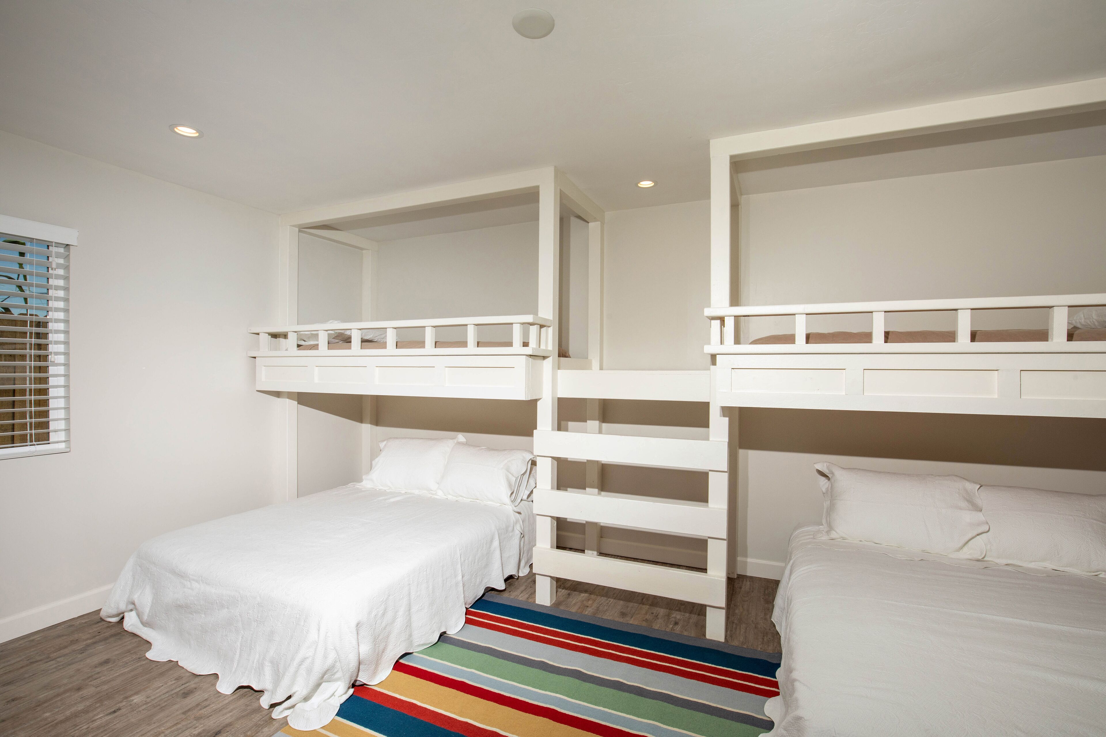 A bedroom with bunk beds, a striped rug, and a window with blinds.