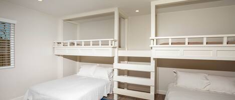 A bedroom with bunk beds, a striped rug, and a window with blinds.