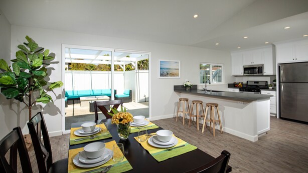 A modern kitchen with white cabinets, a stainless steel refrigerator, and a dining area with a table set for four.