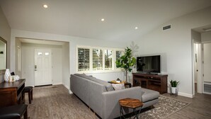 A modern living room with a grey sofa, wooden flooring, a television, and a small table with a plant.