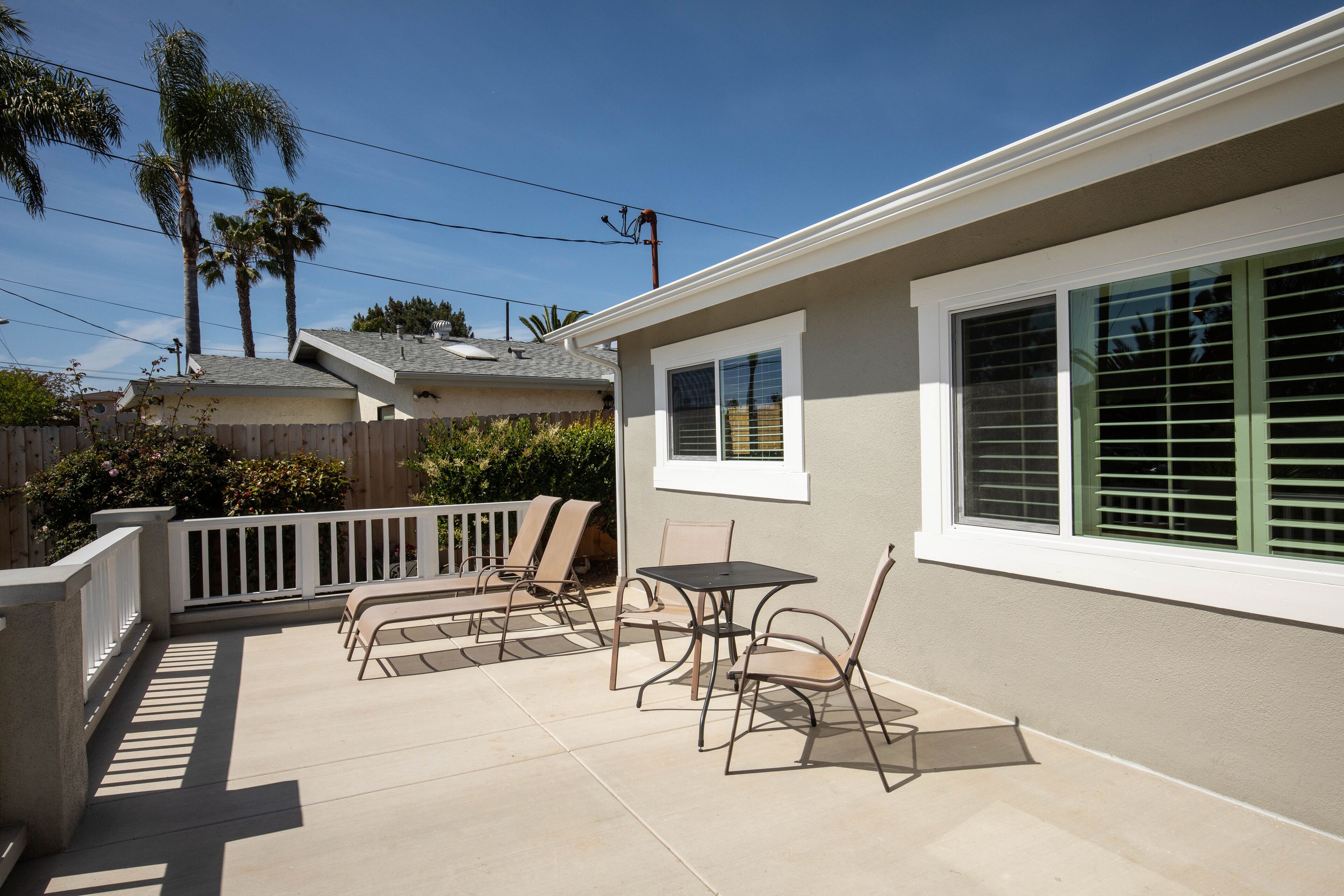 Un patio con mobiliario exterior, baranda blanca y vista a una casa vecina.