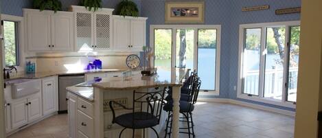 A spacious kitchen with white cabinets, a large island with bar stools, and a view of a lake through the sliding glass doors.