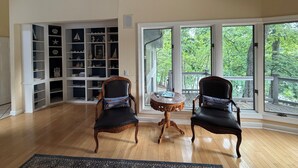 A spacious room with two leather chairs, a small round table, and a large bookshelf filled with various decorative items. - Wind Family Estate--7000sq feet with 7 flex rooms! (Huddleston)