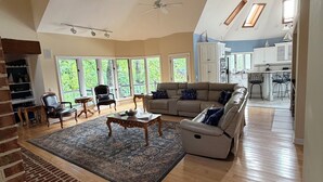 A spacious living room with a fireplace, a sofa, a coffee table, and a view of the kitchen. - Wind Family Estate--7000sq feet with 7 flex rooms! (Huddleston)