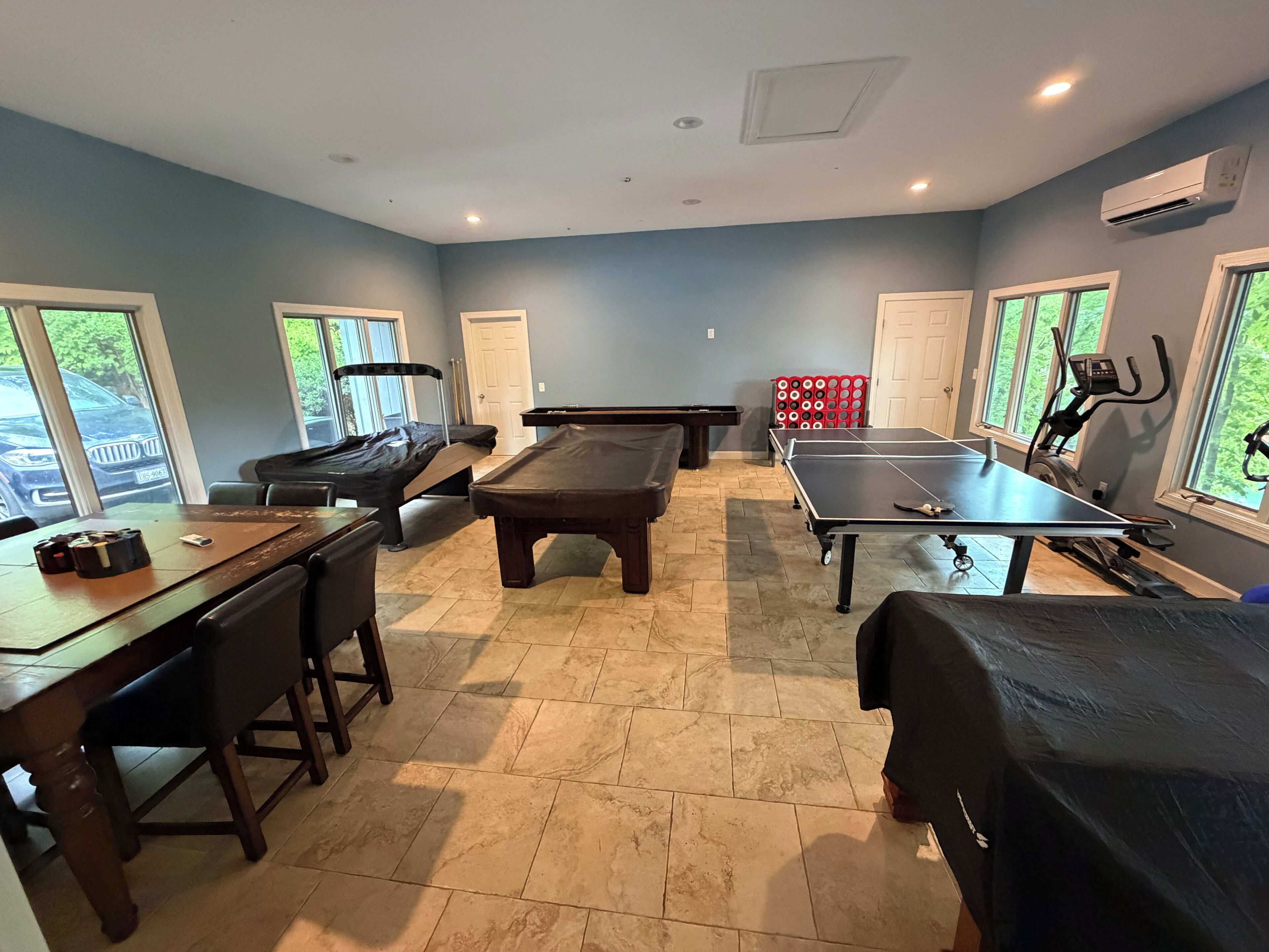 Una habitación con mesa de billar, mesa de ping pong, bicicleta estática y mesa de comedor con sillas.