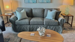 A living room with a grey sofa, two patterned throw pillows, a wooden coffee table with decorative items, a lamp on a side table, and two abstract wall art pieces. - Prime View of Fountain and Channel ~ Great location!   (Grand Haven)