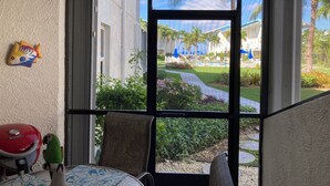 A room with a large window overlooking a pool area, a ceiling fan, and a small table with a chair. - Simply the Best at the Most Reasonable Price-Cayman Reef Resort #2 (George Town)