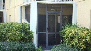 A building with a covered entrance, a small outdoor seating area, and a pathway leading to the entrance. - Simply the Best at the Most Reasonable Price-Cayman Reef Resort #2 (George Town)